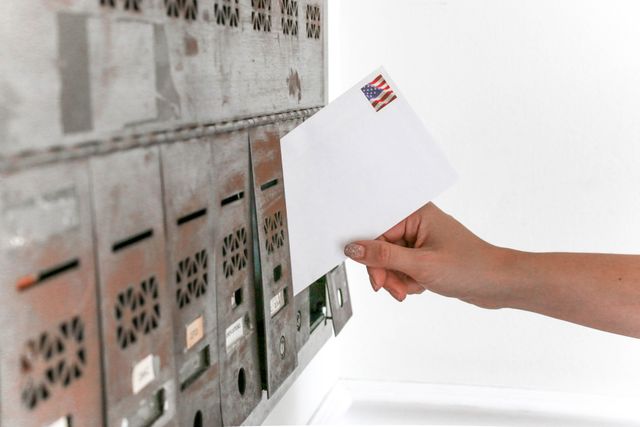 Close-up of a hand inserting a stamped envelope into a mailbox