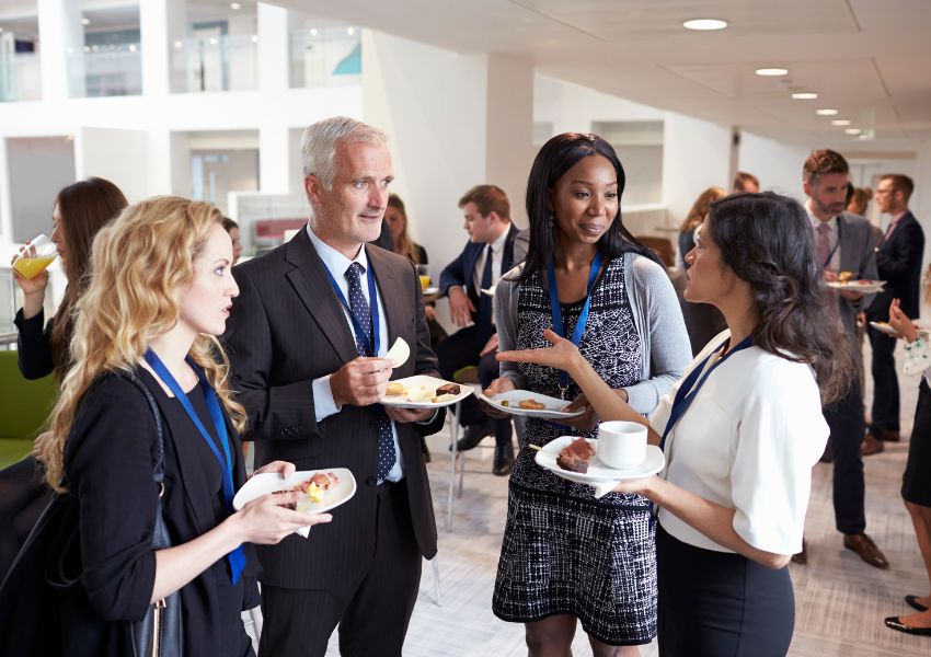 Four rental property investors with lanyards stand and speak about their investments at a networking conference.