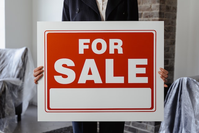 person in a black suit holding a for sale sign